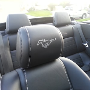 May include: Black leather car seats with white stitching. The driver's seat headrest has a silver embroidered Mustang logo.