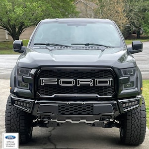 May include: A black Ford F-150 pickup truck with a black grille and a black bumper. The truck has large tires and a black hood. The Ford logo is visible on the grille.