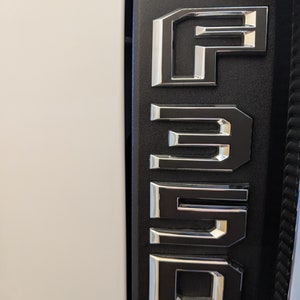 Puede incluir: Primer plano de un emblema Ford F-350 negro y plateado en un vehículo.