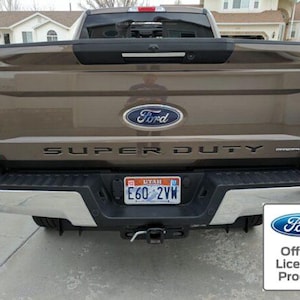 May include: A brown Ford Super Duty pickup truck with a black tailgate and a chrome bumper. The truck has a Utah license plate that reads "E60 2YM". The truck is parked on a paved surface.