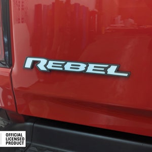 May include: A red truck with a white "Rebel" emblem on the back. The emblem is made of plastic and has a black outline. The truck also has a black bumper with a Mopar logo and the text "Official Licensed Product".