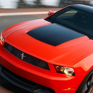 Puede incluir: Un Ford Mustang Boss 302 rojo con una franja de carreras negra en el capó. El coche tiene un parachoques delantero negro y ruedas negras.