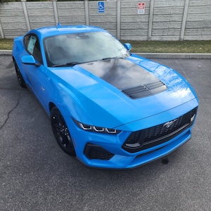 Puede incluir: Un Ford Mustang azul brillante con una franja de carreras negra y una parrilla negra. El coche tiene un alerón negro y ruedas negras.