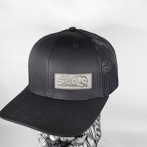 May include: Black baseball cap with a mesh back and a curved brim. The cap features a rectangular patch with the text "426 MOPAR" and a stylized elephant logo.
