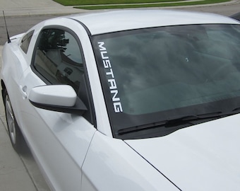 May include: White Ford Mustang with a black windshield and a white "Mustang" decal on the driver's side A-pillar.