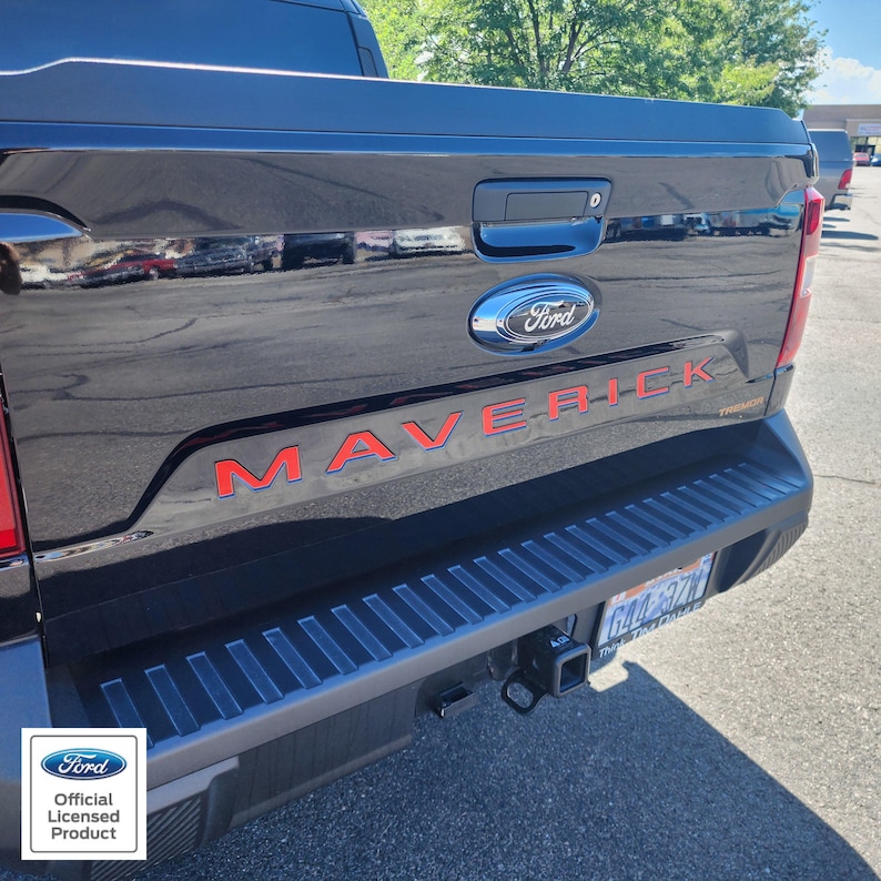 May include: Black Ford Maverick truck tailgate with red "MAVERICK" lettering and a blue Ford emblem. The truck has a black bumper and a trailer hitch. The image includes the "Ford Official Licensed Product" logo.