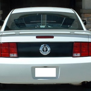 May include: White Ford Mustang with a black racing stripe and a chrome Mustang emblem on the rear. The car has a rear spoiler and red taillights.