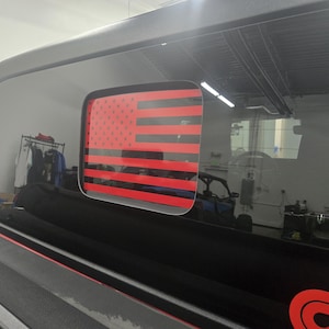 Può includere: Un veicolo nero con un adesivo della bandiera americana rosso, bianco e blu sul lunotto posteriore.