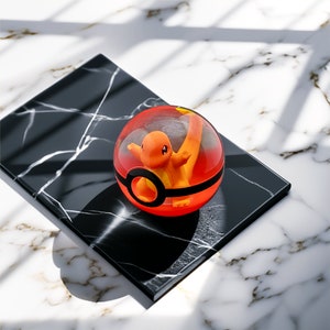 Könnte beinhalten: Ein durchsichtiger, rot-schwarzer Pokéball mit einer orangefarbenen Charmander-Figur im Inneren. Der Ball liegt auf einem schwarzen Marmorquadrat mit weißen Adern. Der Hintergrund ist eine weiße Marmoroberfläche.