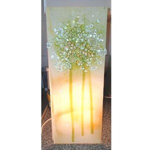 May include: A rectangular, illuminated glass art piece featuring a tree design. The artwork has a light green and yellow color scheme, with a textured, abstract tree composed of green glass pieces. The tree's trunk is represented by three vertical yellow lines.