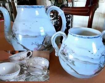May include: A white porcelain tea set with a landscape design. The set includes a teapot, a sugar bowl, and several teacups and bowls. The design features mountains, trees, and birds, with blue trim.