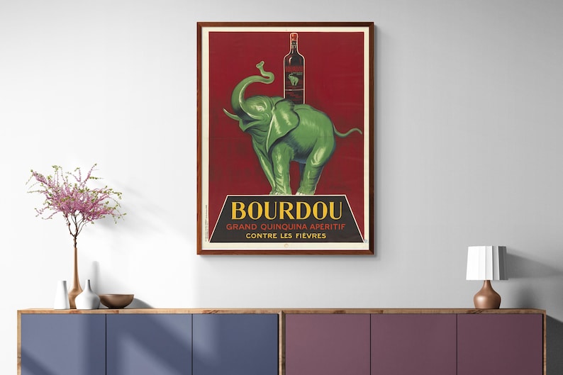 以下が含まれることがあります： ブルドー・グラン・キニーナ・アペリティフのヴィンテージポスター。赤ワインベースのドリンクです。ポスターには、ブルドーのボトルを背負った緑色の象が後ろ足で立っている様子が描かれています。ポスターのテキストには、「ブルドー・グラン・キニーナ・アペリティフ・コントル・レ・フィエーブル」と書いてあります。