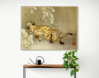 Puede incluir: Una impresión de arte japonesa vintage que representa un tigre amarillo y marrón saltando a través de un paisaje nevado. El tigre está mirando hacia el lado izquierdo de la imagen y tiene la boca abierta. El fondo es de color marrón claro con nieve blanca cayendo. La impresión está enmarcada en un marco de madera marrón claro.