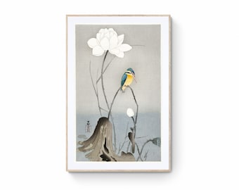 Op de afbeelding: Een Japanse stijl schilderij van een blauwe en gele vogel die op een tak zit met een witte lotusbloem. De achtergrond is zacht grijs.