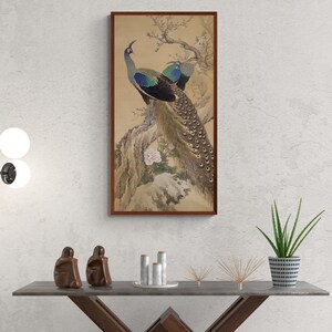 May include: A framed painting of two peacocks perched on a branch with a pink flower. The peacocks have blue and green feathers and are surrounded by brown branches and leaves.