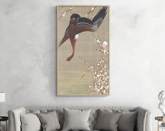 Puede incluir: Una impresión japonesa vintage en madera que representa un pájaro marrón y negro con la cabeza inclinada, posado en una rama con flores blancas que parecen nieve. El fondo es de color beige suave con un patrón sutil.