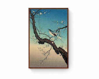May include: A framed print of a Japanese woodblock artwork. The print depicts a small bird perched on a flowering tree branch. The background transitions from a light beige to a deep blue, creating a serene and natural scene.