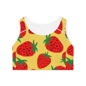 May include: A yellow sports bra with a repeating pattern of large red strawberries with green leaves and black seeds. The bra has a white trim around the neckline and armholes.