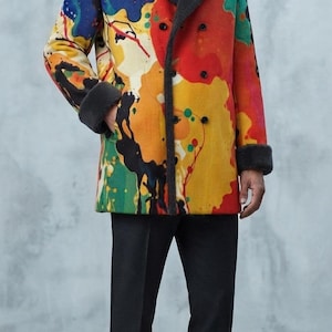 Puede incluir: Un abrigo de doble botonadura con un patr&oacute;n de salpicaduras de pintura multicolor en rojo, amarillo, azul y verde. El abrigo tiene cuello y pu&ntilde;os de piel sint&eacute;tica gris oscuro, combinado con un su&eacute;ter de cuello alto y pantalones gris oscuro.