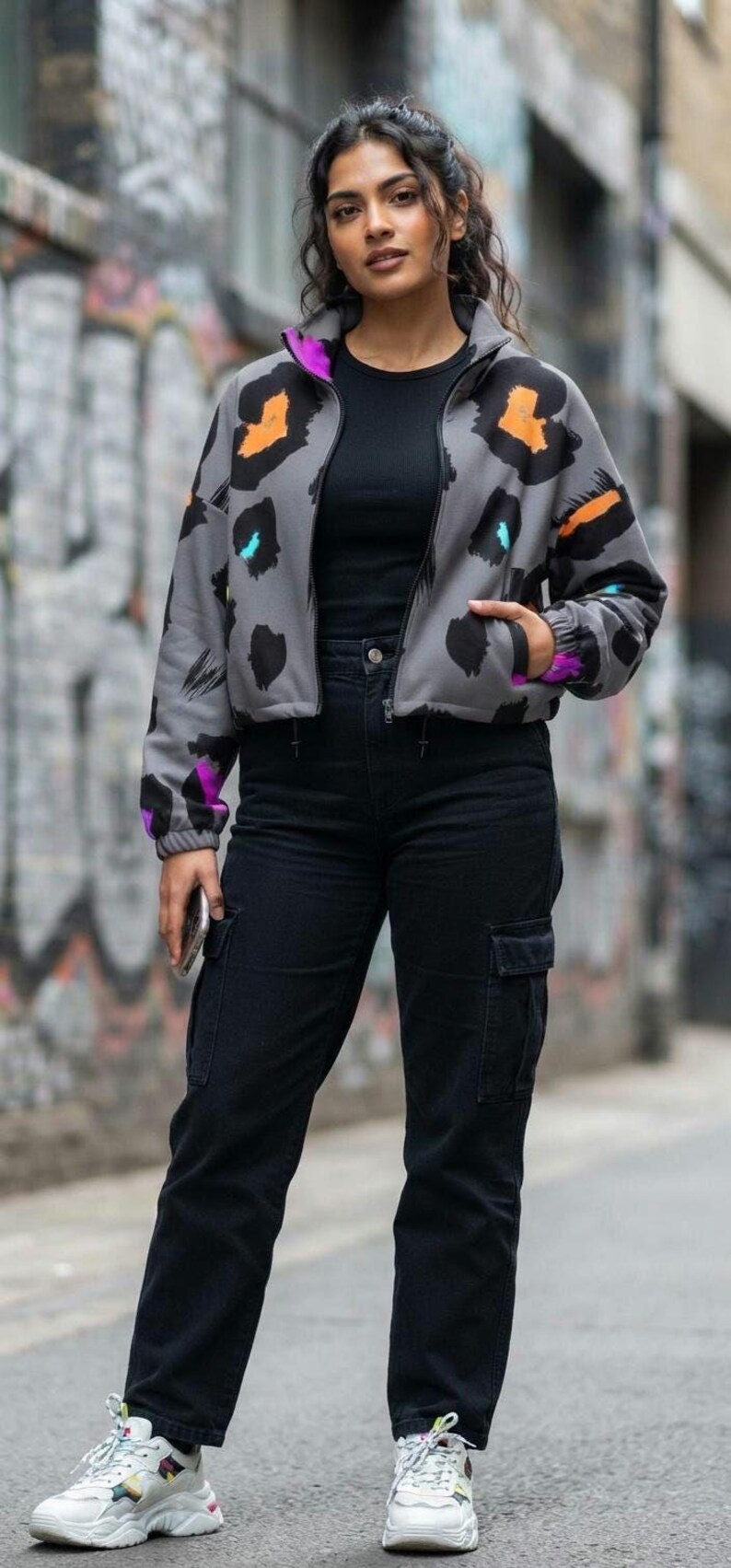 May include: A gray zip-up jacket featuring a black, orange, and purple abstract animal print pattern, worn over a black t-shirt with black cargo pants and white sneakers with colorful accents. The jacket has a high collar and elastic cuffs.