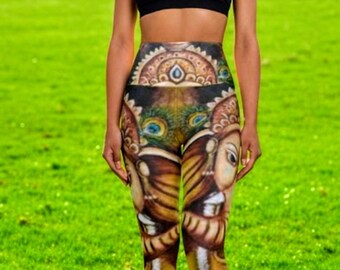 Puede incluir: Una mujer con un sujetador deportivo negro y leggings estampados. Los leggings muestran un diseño detallado con pavo real y patrones ornamentados en marrón, dorado y azul. El fondo es un campo de hierba verde.