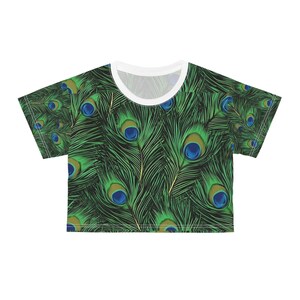 May include: A cropped t-shirt featuring a vibrant peacock feather pattern. The design showcases a repeating pattern of green feathers with blue and gold eye-like details. The shirt has a white neckline and short sleeves.