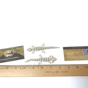 May include: Two beige plastic gecko skeletons, each about 6 inches long, are displayed on a white surface. A ruler is visible in the bottom of the image. A business card with the text "Gavin Schatz Content Creator" is visible in the lower left corner of the image. A card with a QR code and the text "Use the QR code to subscribe to my channel TINYURL.COM/GAVINYOUTUBE" is visible in the upper right corner of the image.