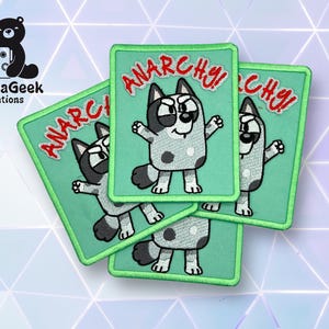 Puede incluir: Parches bordados con un personaje de perro de dibujos animados y la palabra "ANARCHY!" en rojo. Los parches tienen un fondo y un borde verde claro. Los parches están apilados unos sobre otros.