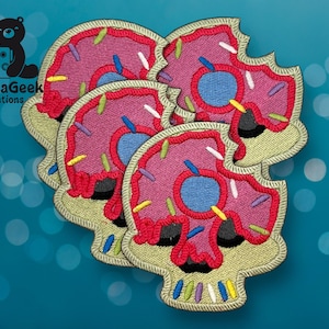 May include: Embroidered patches in the shape of a skull, designed to look like a pink frosted donut with colorful sprinkles. The patches have a light green border and a blue center. The patches are stacked on top of each other.