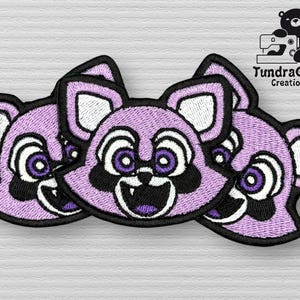 Op de afbeelding: Drie paarse geborduurde patches met een cartoon dierengezicht. Elke patch heeft een witte omtrek en zwarte ogen met paarse pupillen. Het dier heeft een brede, tanden grijns.