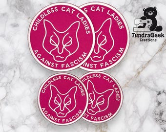 May include: Four pink and white embroidered iron-on patches with a cat design and the text "Childless Cat Ladies Against Fascism".