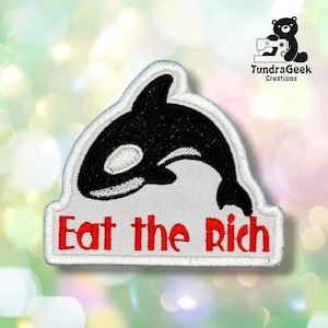 Può includere: Una toppa ricamata raffigurante un'orca nera e bianca sopra il testo rosso "Eat the Rich". La toppa presenta uno sfondo bianco con un bordo bianco e una base rettangolare piatta con un bordo superiore curvo.