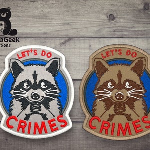 May include: Two embroidered patches featuring a cartoon raccoon with the text "Let's Do Crimes". The raccoon is holding a gun in its paws. One patch is white with red text and the other is tan with red text.