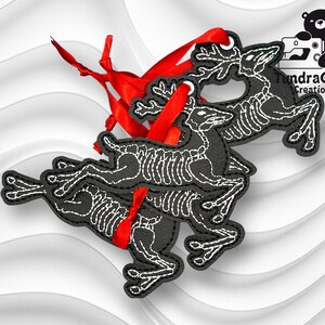 以下が含まれることがあります： 赤いリボンが付いた黒いスケルトン鹿のオーナメント3つ。鹿は積み重ねられており、一番上の鹿の角が見えています。