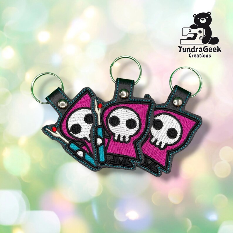 Three identical Seam Reaper keychains fanned out together, each on a green metal split ring, showing the same hooded skull and seam ripper design.