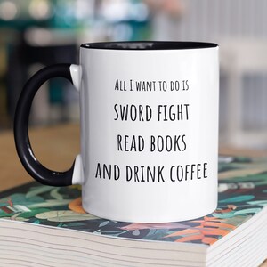 May include: White coffee mug with a black handle and black rim. The mug has the text "All I want to do is sword fight read books and drink coffee" printed on it.