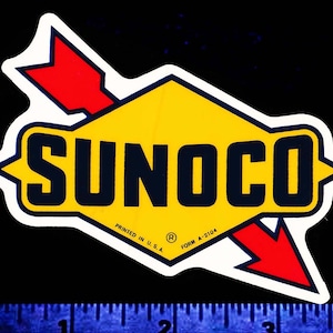 May include: A white sticker with a yellow diamond shape containing the word "SUNOCO" in black letters. A red arrow points to the right, with the text "PRINTED IN U.S.A. FORM A-2104" below the diamond.