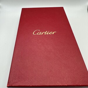 May include: A red Cartier box. The box is rectangular and made of a textured material. The Cartier logo is embossed in gold on the front of the box. The box is a deep, rich red color.  The box is likely used for packaging luxury goods. The box is shown from a slightly elevated angle, showcasing its top surface and sides.