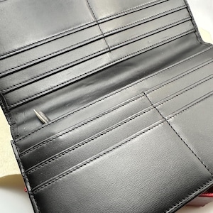 May include: A black leather Cartier Paris wallet is open, showcasing multiple card slots and compartments.  The interior is neatly stitched, and the brand name is subtly embossed on the bottom.  The wallet appears to be made of high-quality leather with a smooth finish. A silver pen is partially visible in one of the compartments.