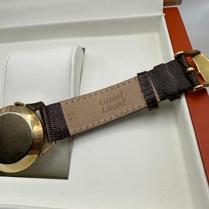 Puede incluir: Una correa de reloj de cuero marr&oacute;n con el texto "Grand Lizard" grabado en el interior.