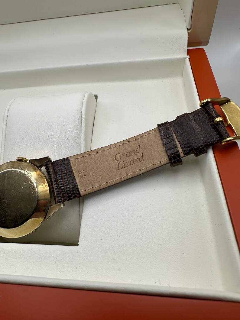 Puede incluir: Una correa de reloj de cuero marr&oacute;n con el texto "Grand Lizard" grabado en el interior.