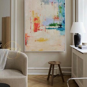 Peut inclure: Peinture abstraite avec des coups de pinceau color&eacute;s dans des tons de rouge, bleu, vert, jaune et blanc sur une toile cr&egrave;me. La peinture est encadr&eacute;e dans un cadre blanc et est accroch&eacute;e &agrave; un mur dans un salon.