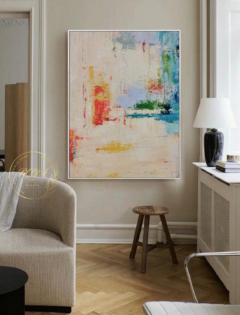 Peut inclure: Peinture abstraite avec des coups de pinceau color&eacute;s dans des tons de rouge, bleu, vert, jaune et blanc sur une toile cr&egrave;me. La peinture est encadr&eacute;e dans un cadre blanc et est accroch&eacute;e &agrave; un mur dans un salon.