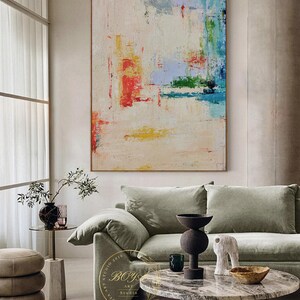 Peut inclure: Peinture abstraite sur fond blanc avec des coups de pinceau color&eacute;s dans des tons de rouge, bleu, vert et jaune. La peinture est accroch&eacute;e &agrave; un mur dans un salon avec un canap&eacute; vert et une table basse en marbre.