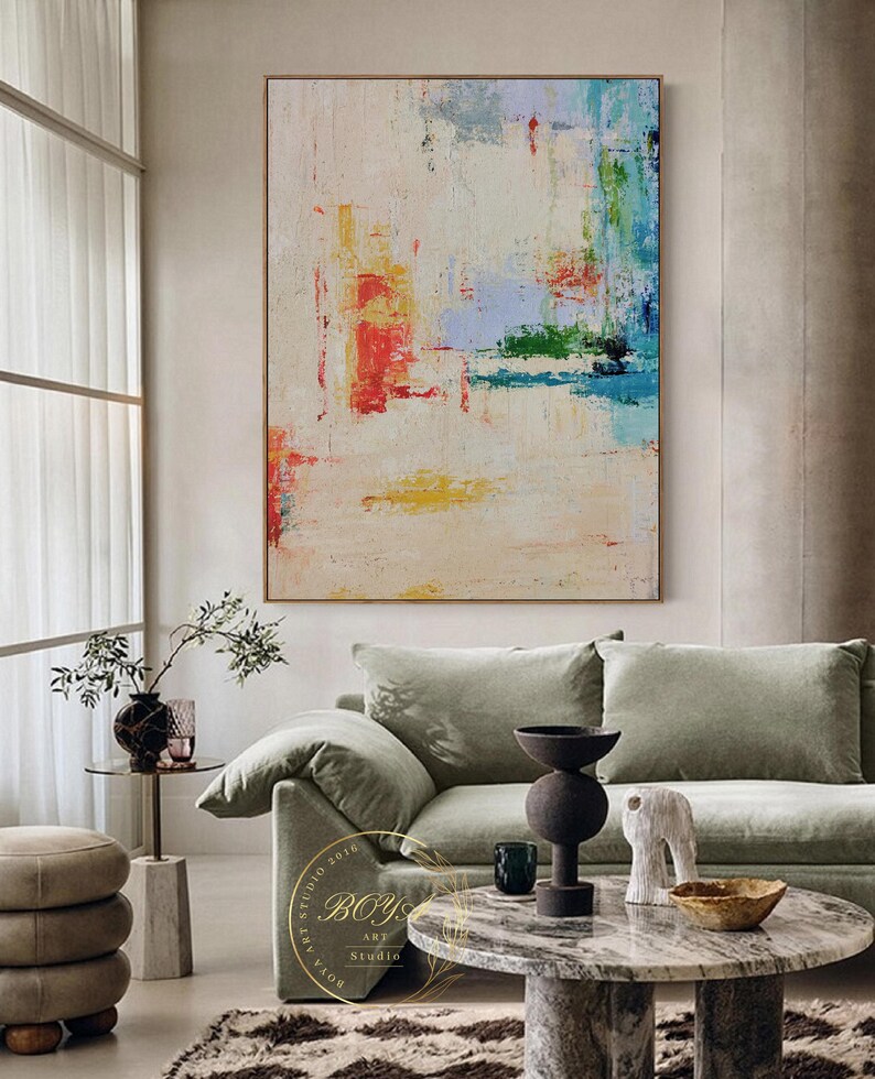 Peut inclure: Peinture abstraite sur fond blanc avec des coups de pinceau color&eacute;s dans des tons de rouge, bleu, vert et jaune. La peinture est accroch&eacute;e &agrave; un mur dans un salon avec un canap&eacute; vert et une table basse en marbre.