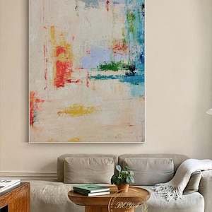 Peut inclure: Peinture abstraite sur fond blanc avec des coups de pinceau color&eacute;s dans des tons de rouge, bleu, vert et jaune. La peinture est accroch&eacute;e au mur au-dessus d'un canap&eacute; beige.