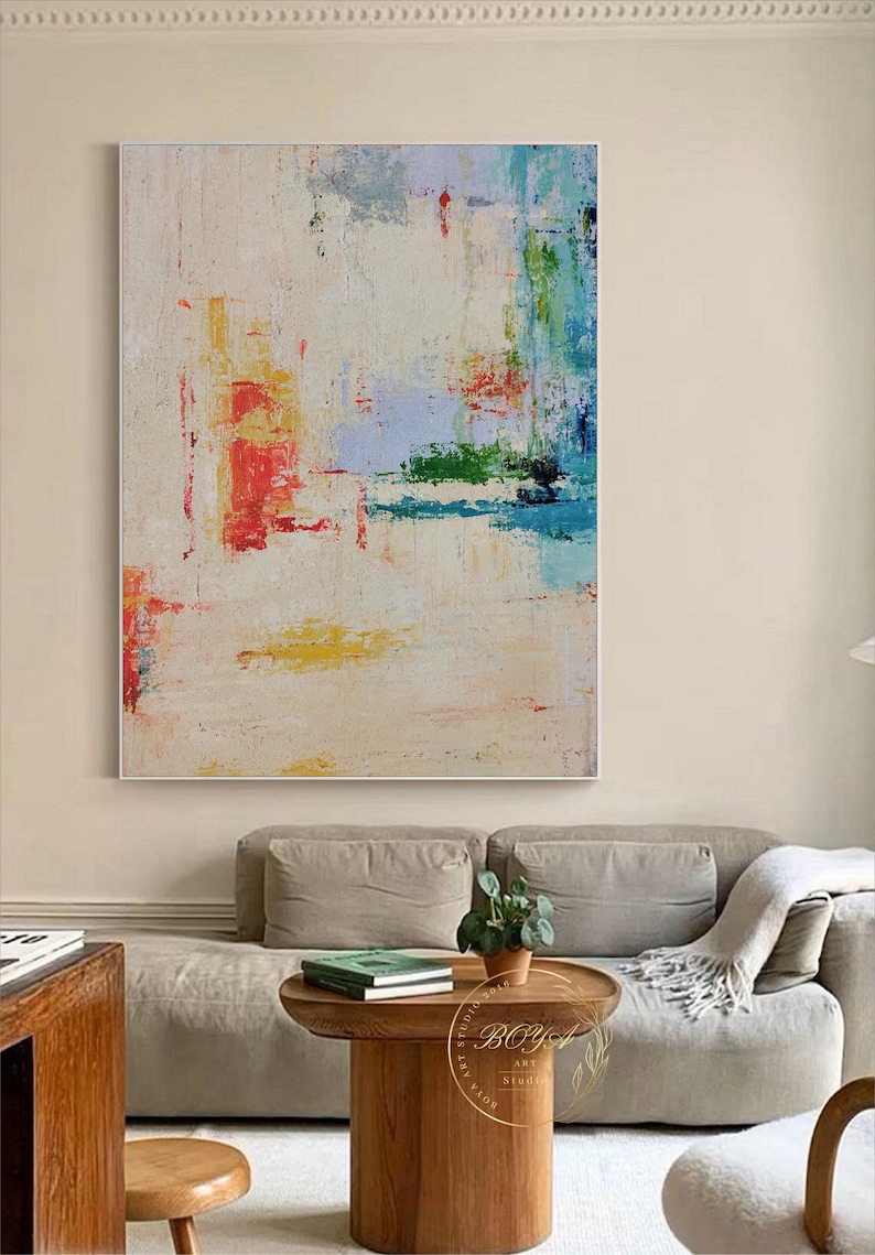 Peut inclure: Peinture abstraite sur fond blanc avec des coups de pinceau color&eacute;s dans des tons de rouge, bleu, vert et jaune. La peinture est accroch&eacute;e au mur au-dessus d'un canap&eacute; beige.