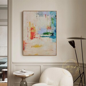 Peut inclure: Peinture abstraite sur fond blanc avec des coups de pinceau color&eacute;s dans des tons de bleu, vert, jaune et rouge. La peinture est encadr&eacute;e d'un cadre fin et dor&eacute;.