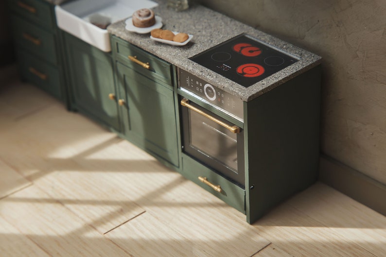 Op de afbeelding: Een groene keukenkast met een zwarte oven en een glazen kookplaat. De kookplaat heeft twee rode hete branders. De kast heeft gouden handgrepen.