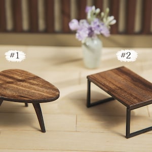 May include: Two miniature wooden tables, one with a rounded, oval top and three legs, and the other with a rectangular top and a black metal frame. The tables are on a light wood surface. #1 and #2 are written above each table.